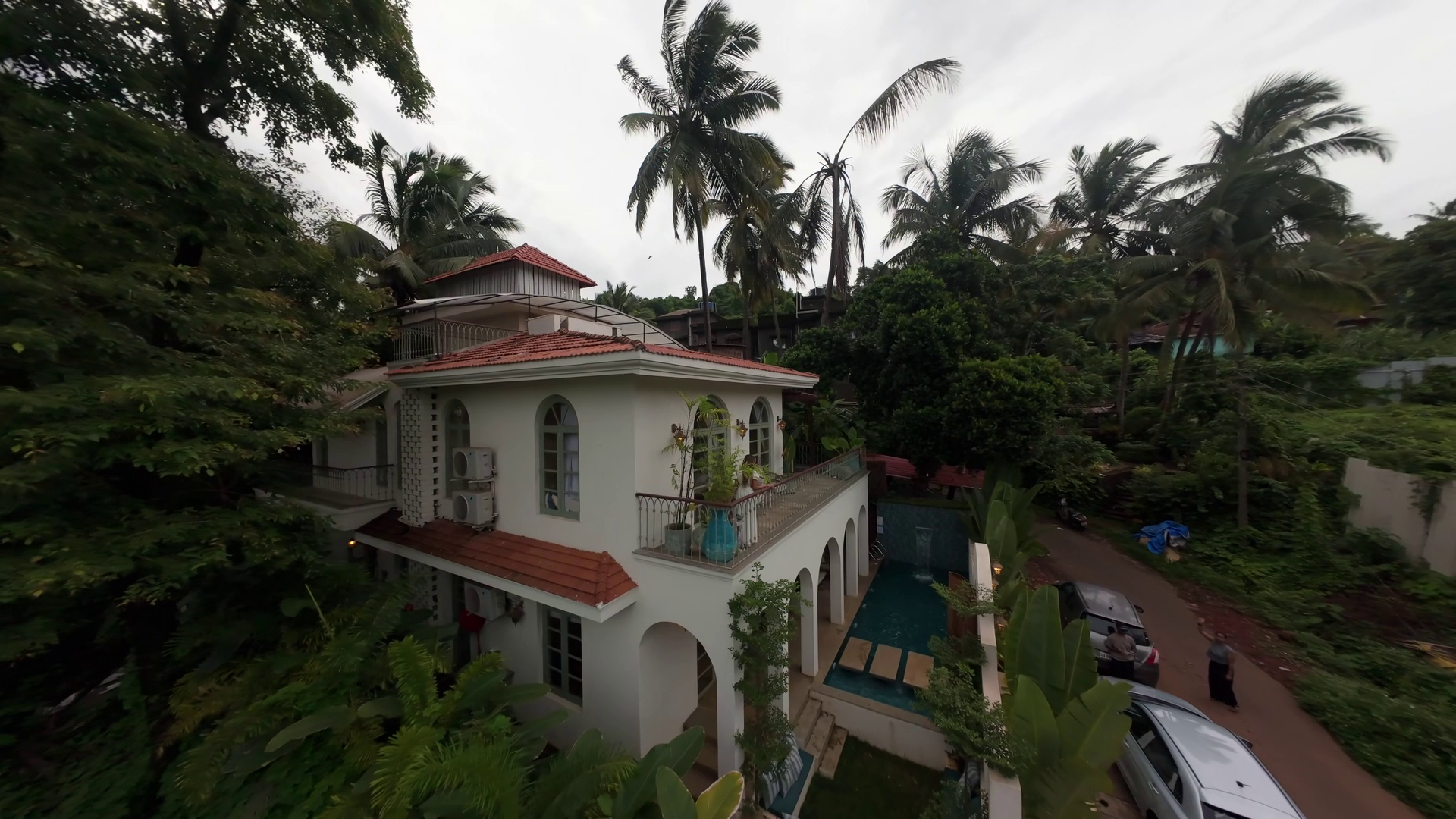 Aerial view of Casa Amore in Bastora — a white Indo-Portuguese villa with a red tiled roof and arched windows, its private pool alongside, surrounded by palms and dense green